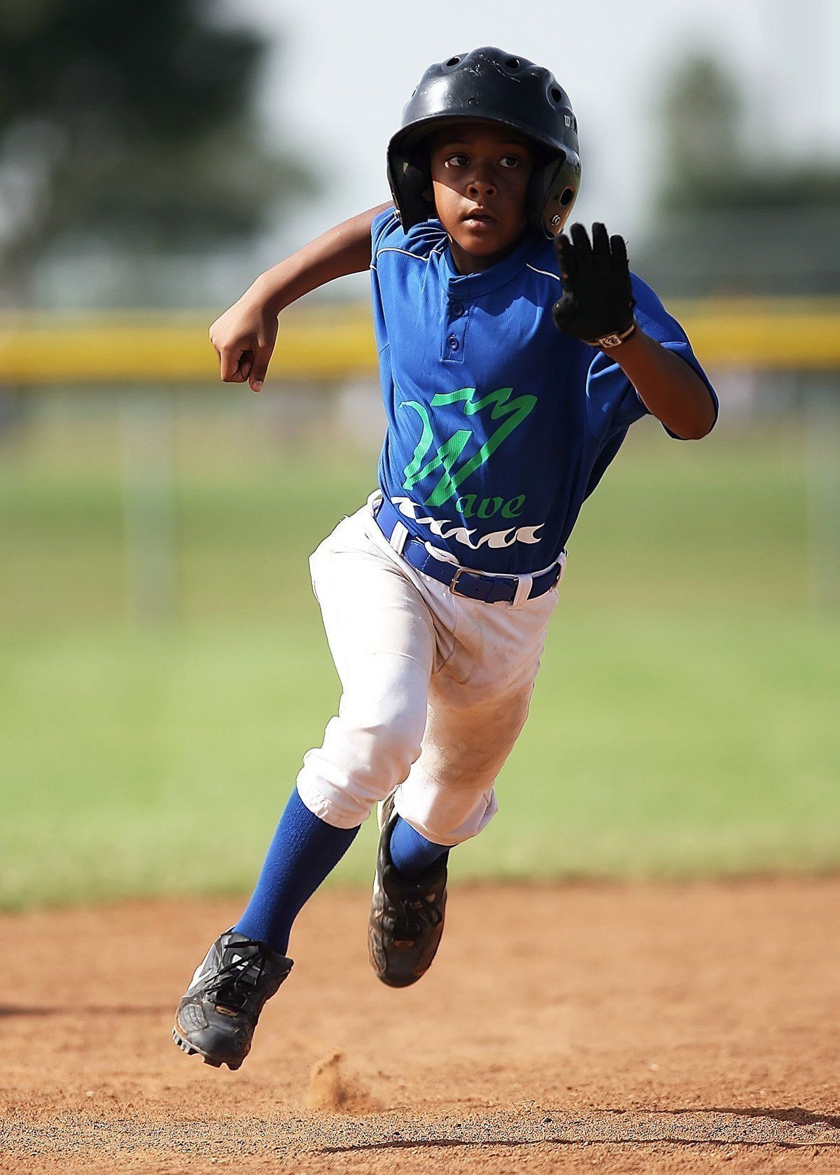 Youth baseball player in blue uniform sprinting on a dirt field, wearing a black helmet and glove.