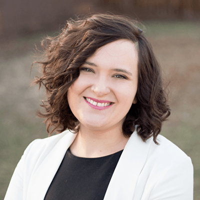 A woman with curly hair and a white jacket is smiling for the camera.