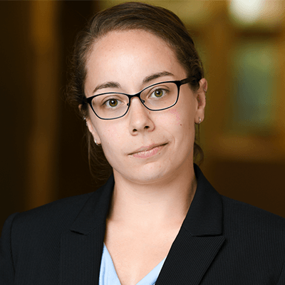A woman wearing glasses and a suit is looking at the camera.