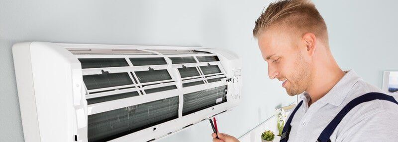 A man is fixing an air conditioner with a pencil - Electrician in Emerald | All Saints Electrical