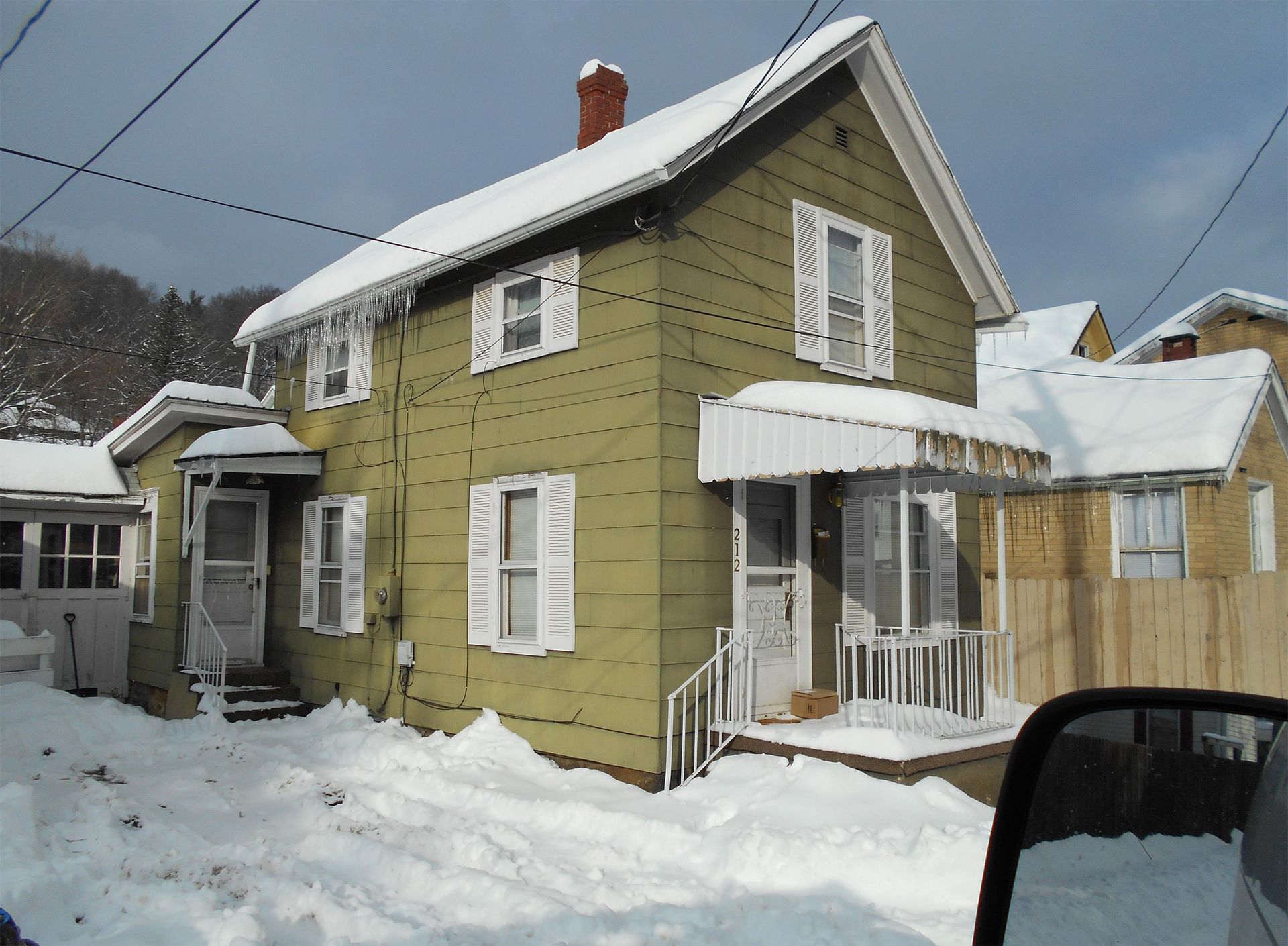 Snow-covered yellow house with white trim and a small porch in a winter neighborhood