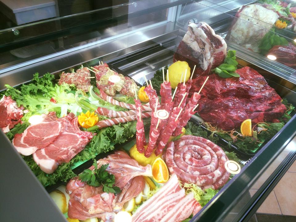 Vetrina con vari tipi di carne cruda, tra cui salsicce, kebab e bistecche, disposte con lattuga e fette di limone.
