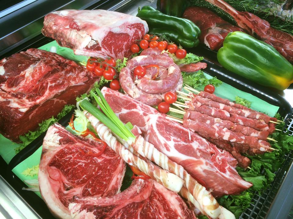 Assortimento di tagli di carne cruda, tra cui bistecche, salsicce e kebab, esposti con verdure.