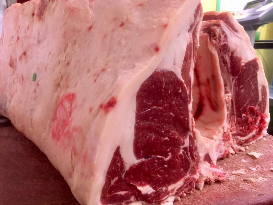 Grandi tagli di carne di manzo cruda, ricoperti di grasso bianco, disposti su una superficie di legno.