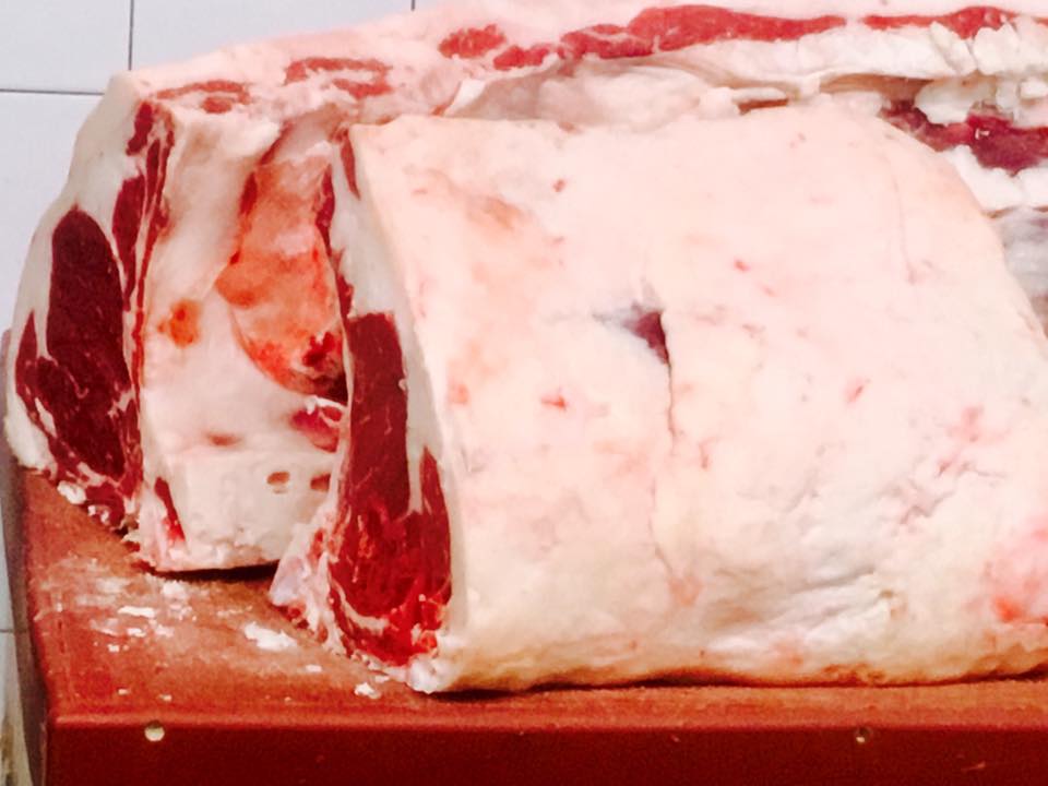 Grandi tagli di manzo crudo, marezzati di grasso, su un tagliere rosso.