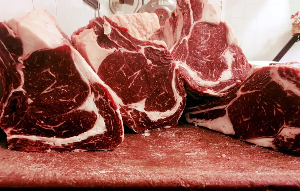 Bistecche di ribeye crude su un tagliere, con venature marmoree e colore rosso.