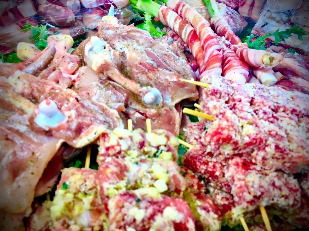 Esposti vari tipi di carni crude: pollame, kebab e prodotti avvolti nella pancetta, pronti per essere cucinati.