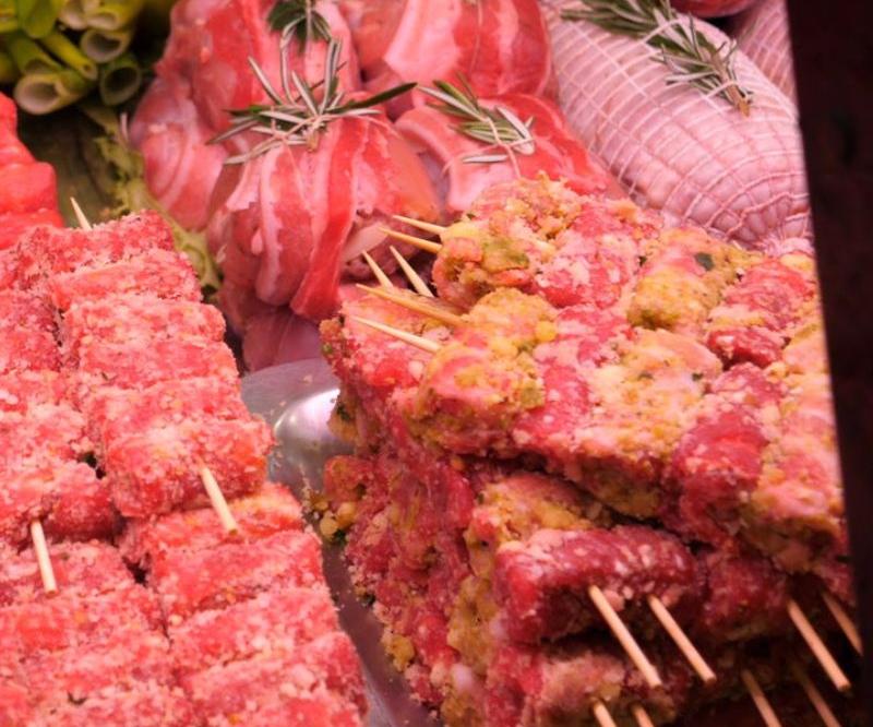 Esposizione di spiedini e tagli di carne cruda, caratterizzati da tonalità rosse e rosa, probabilmente in vendita in una macelleria.