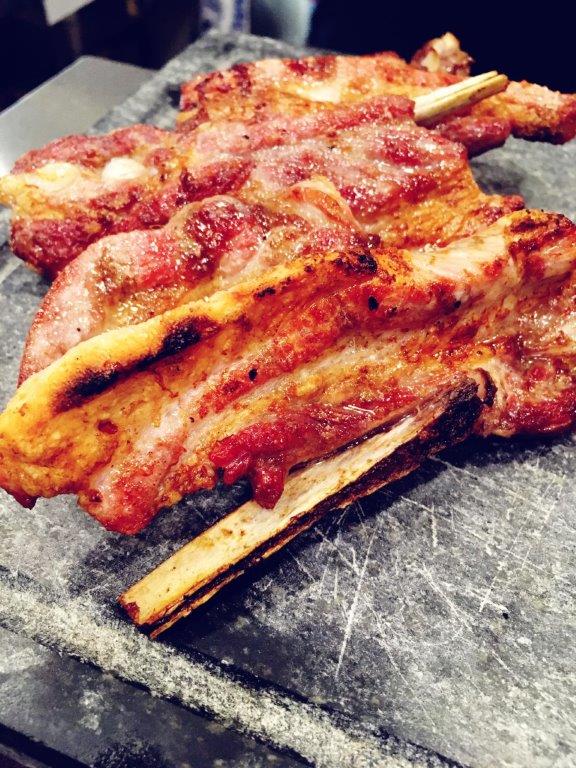 Costolette di agnello grigliate su una lastra di pietra scura e ruvida. Carne rossa, bordi dorati, con osso.