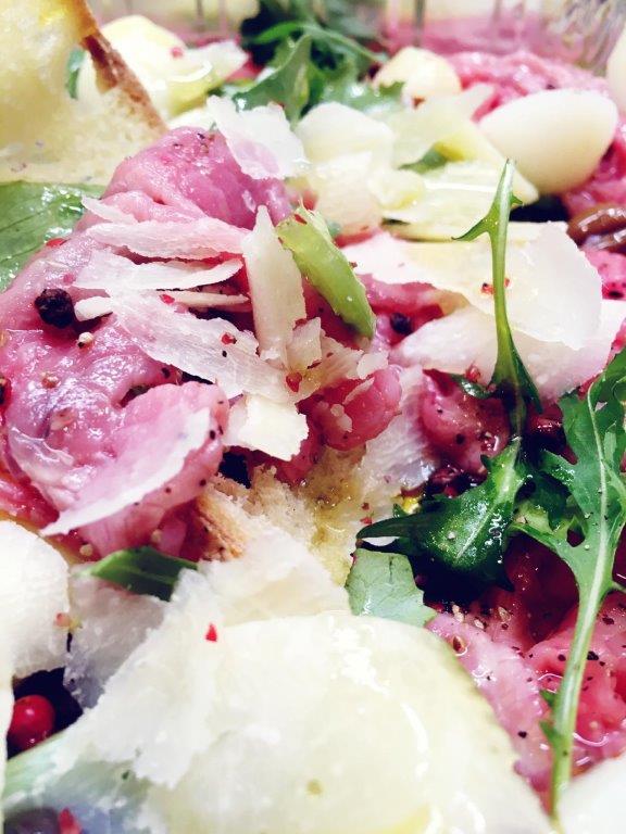 Insalata di carpaccio con formaggio a scaglie, rucola e cipolle bianche.
