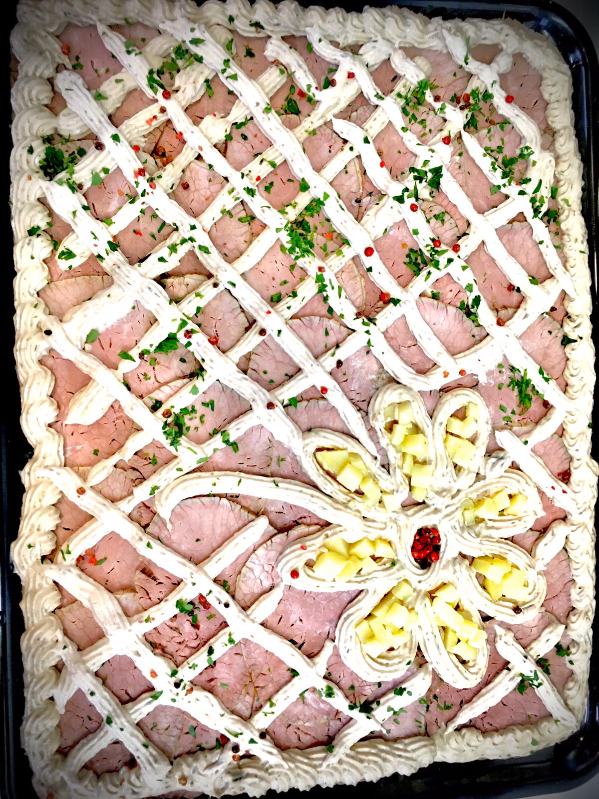 Pagnotta di prosciutto e formaggio con glassa a reticolo e guarnizione di fiori, cosparsa di prezzemolo.