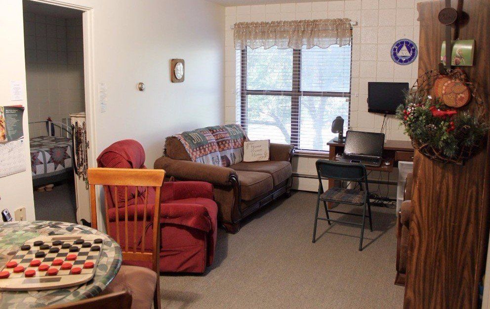 Small living room with couch, desk, chair, window, and checkerboard table.