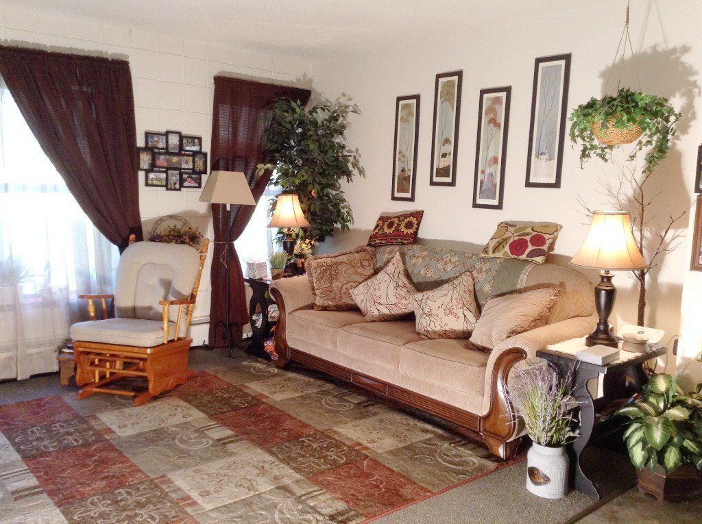 Cozy living room with a couch, armchair, rug, and decorative wall art. Warm colors and lamp lighting.