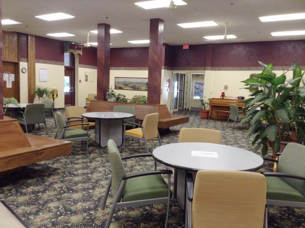 Lounge area with tables, chairs, and potted plants. Walls are burgundy and beige, with a patterned carpet.