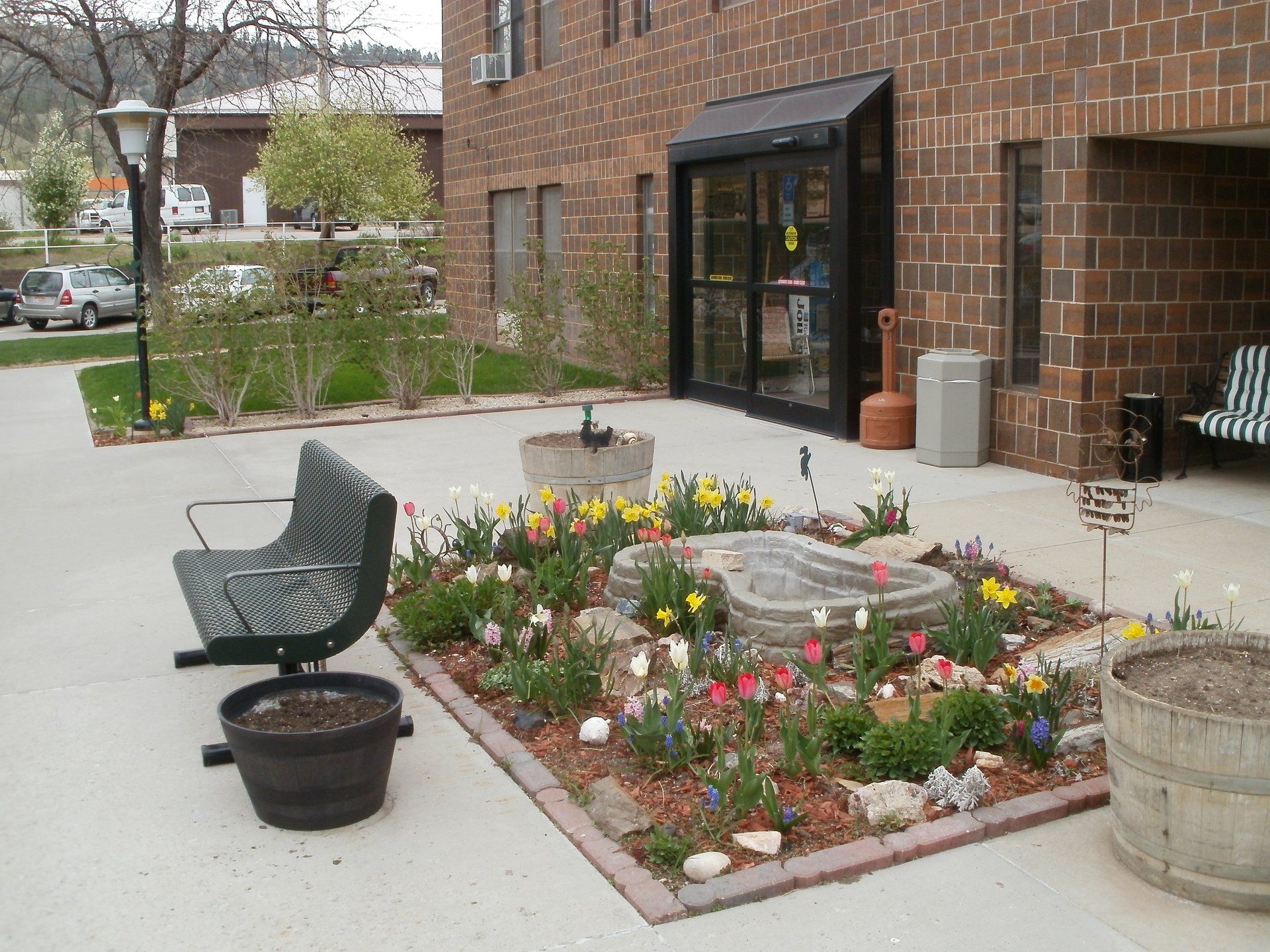 Brick building entrance with flowerbeds, benches, and a small water feature.