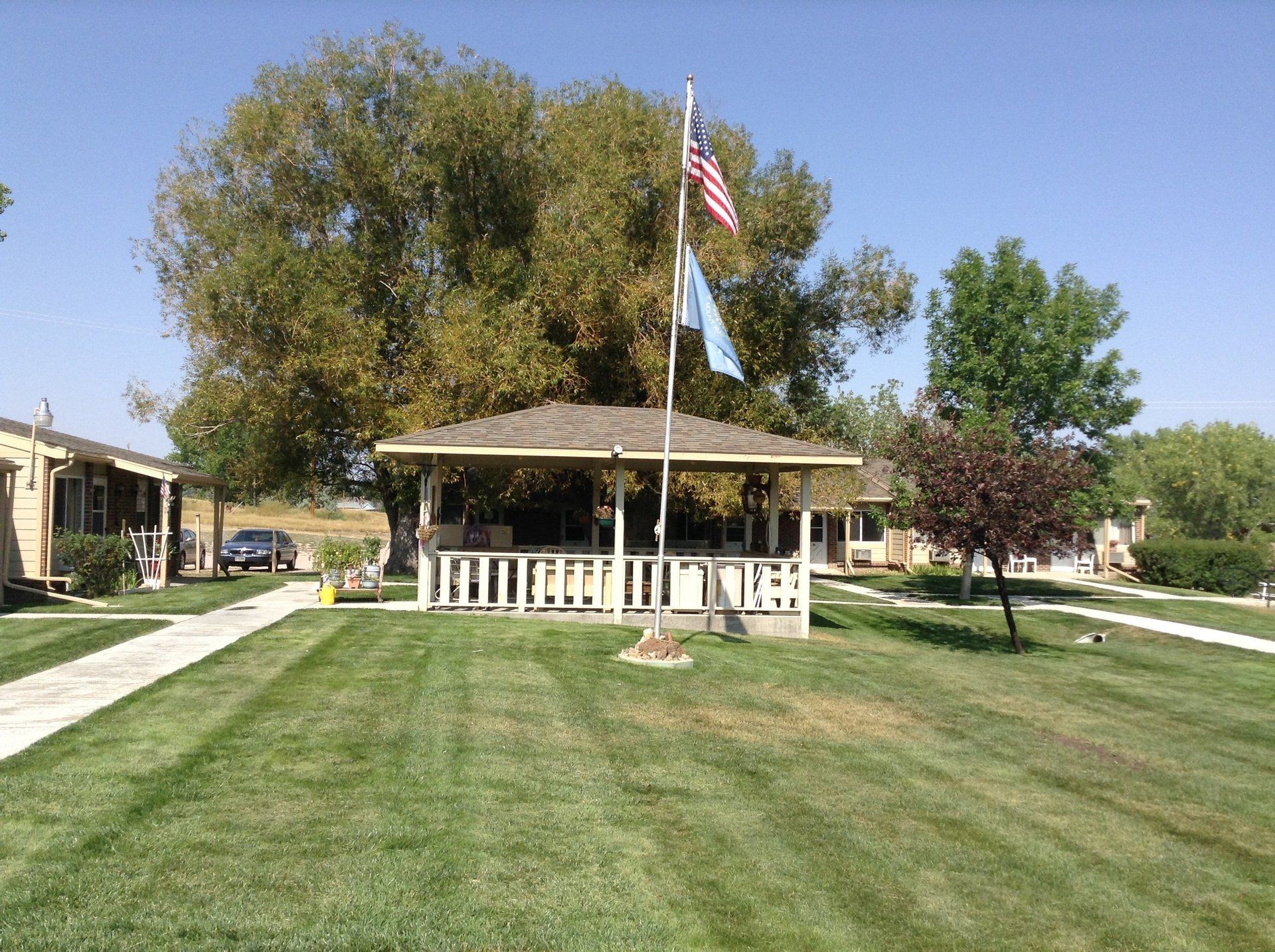 Gazebo with American flag and another flag, lawn, trees, buildings in background.