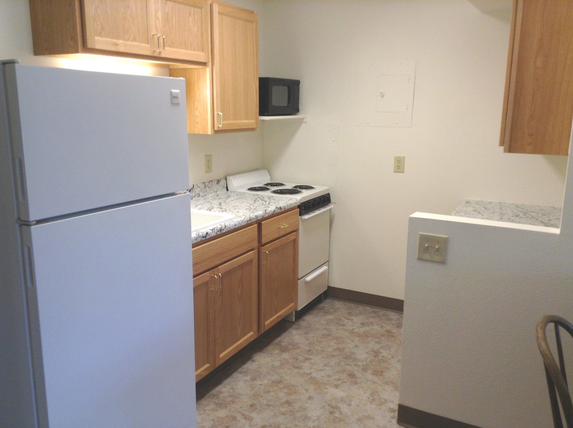 A small kitchen with light wood cabinets, white appliances, and granite countertops.