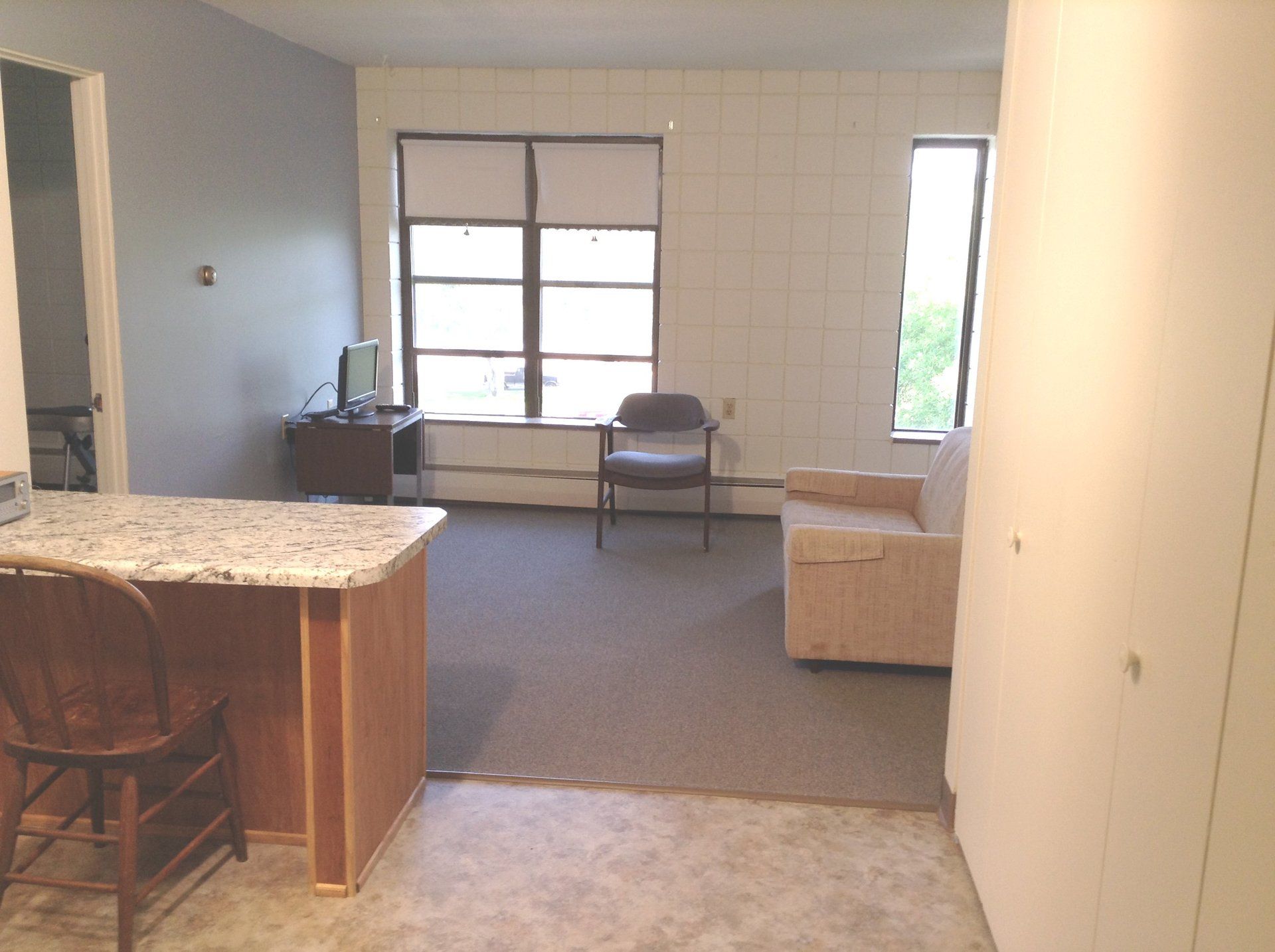 Living space with kitchen counter, sofa, chair, and large windows.
