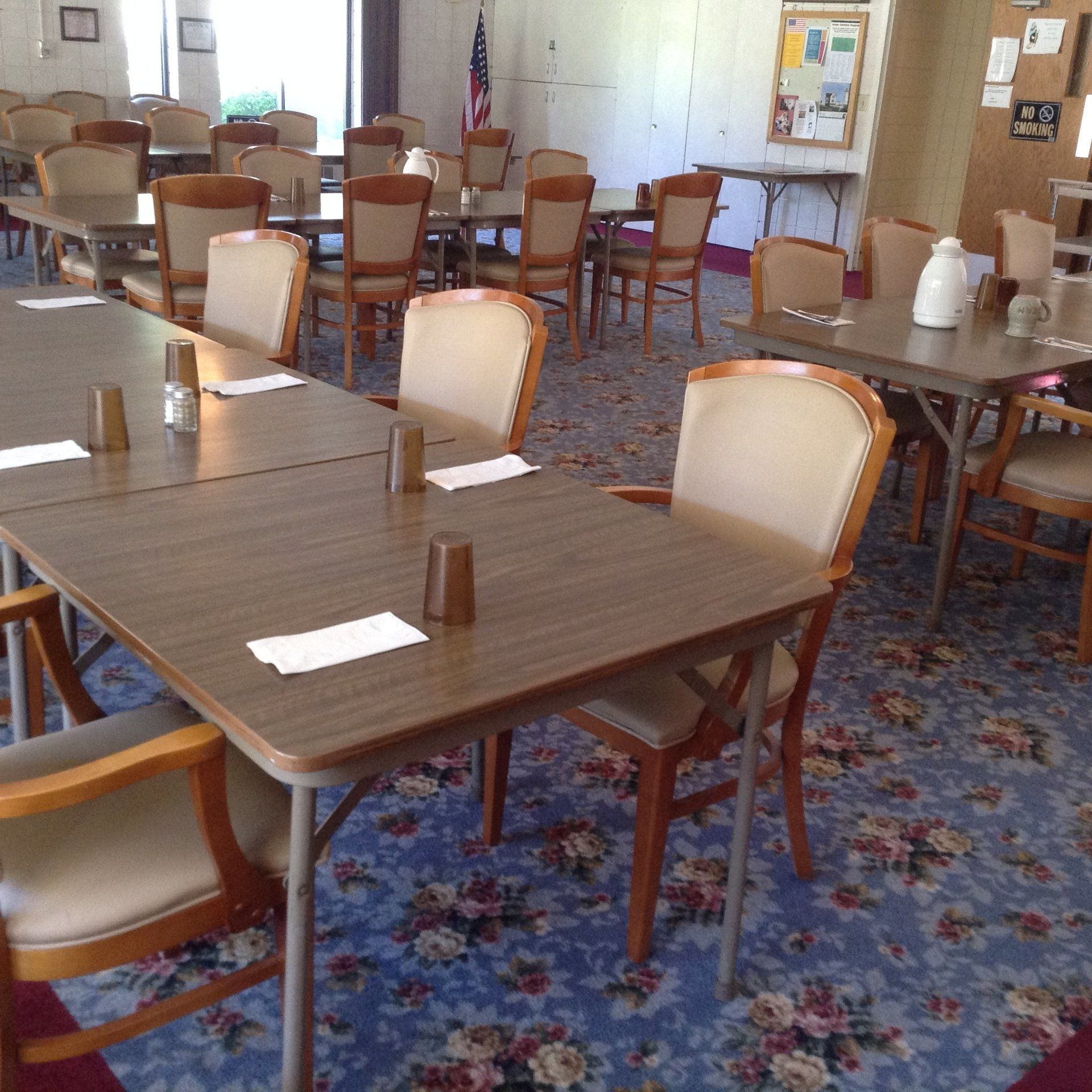 Dining room with tables set for a meal; chairs arranged; floral carpet.
