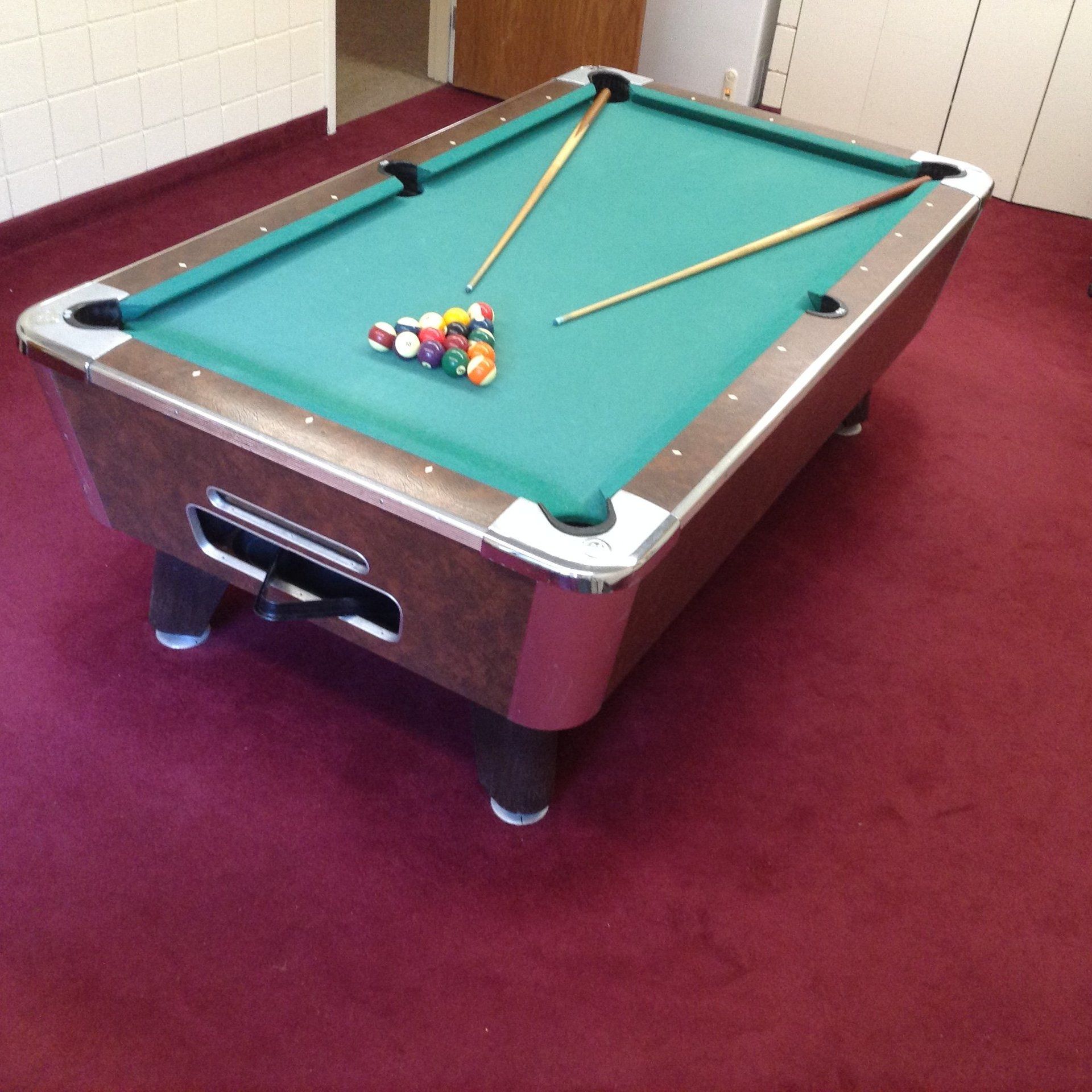 Pool table with balls racked, two cues, on red carpet, room setting.
