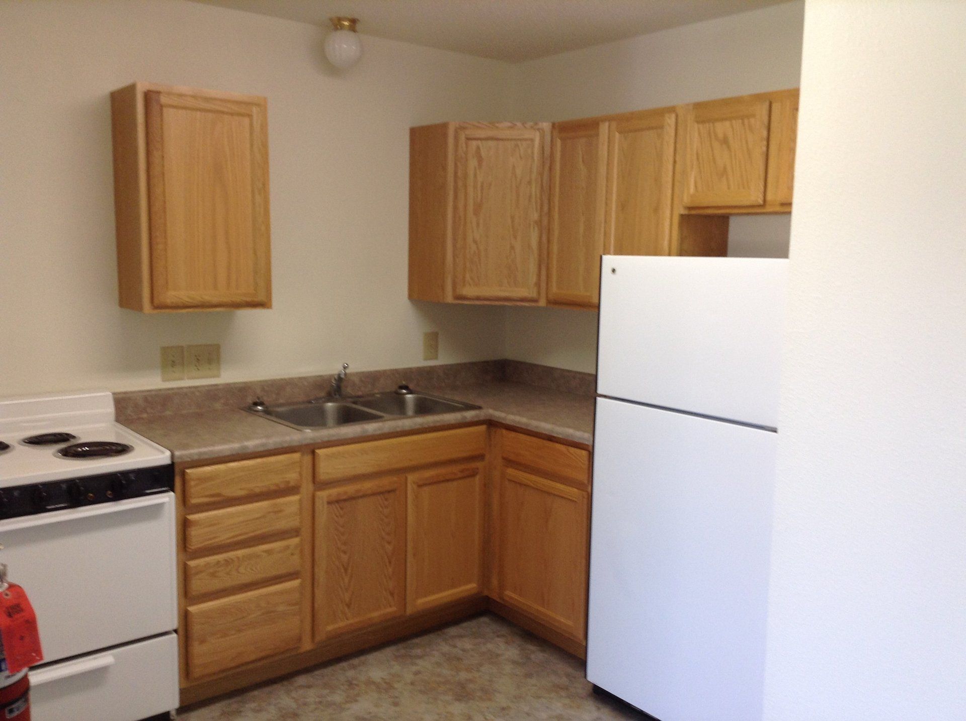 Small kitchen with light-colored cabinets, a white refrigerator, stove, and double sink.