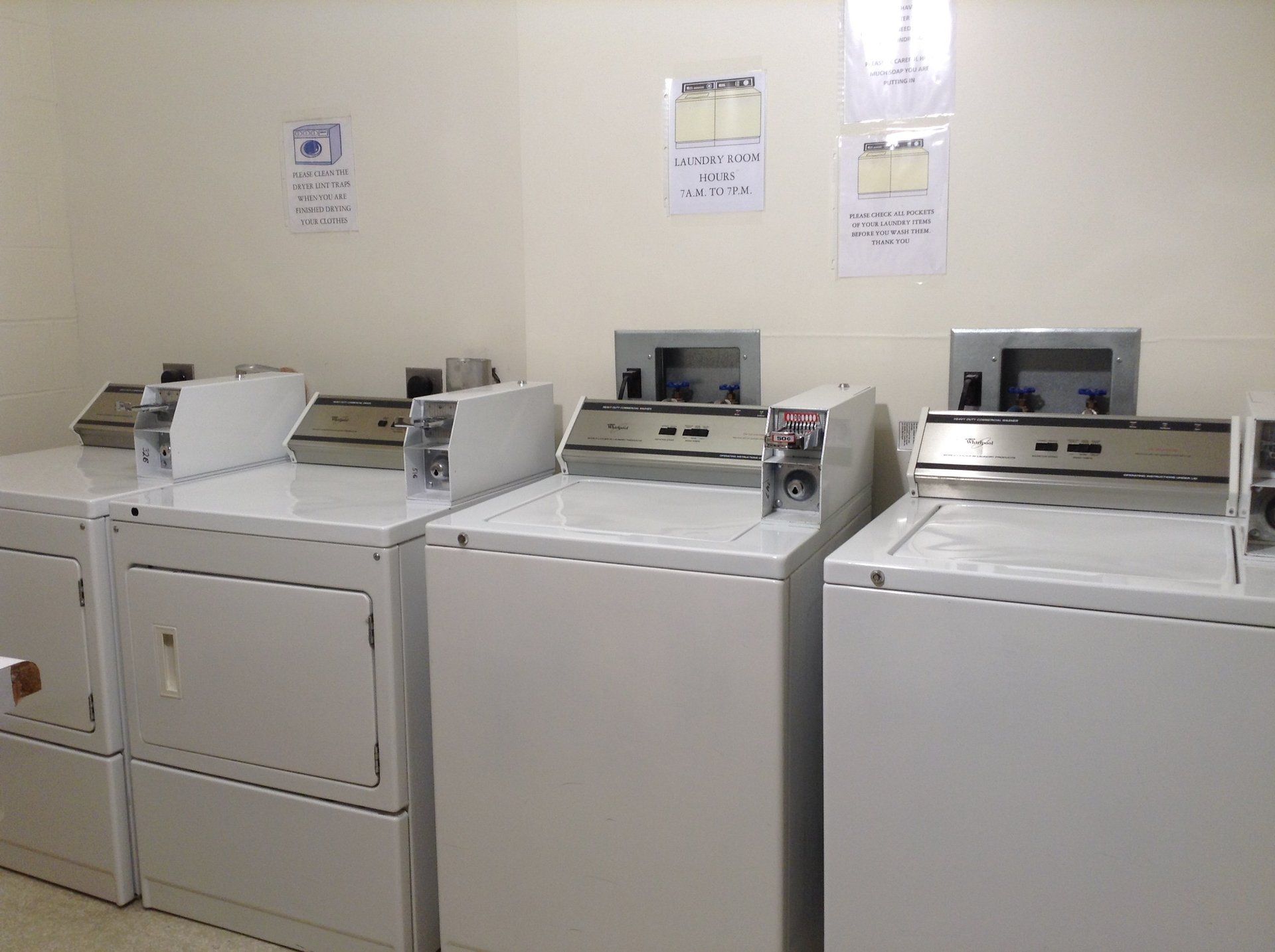 Row of white washing machines in a laundry room, with signs on the wall.