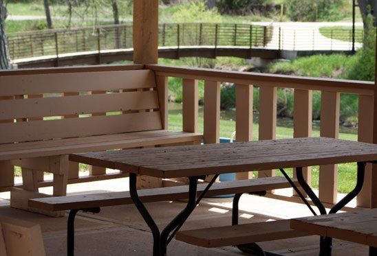 Picnic tables and benches in a covered pavilion overlooking a footbridge and creek.