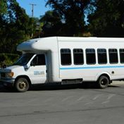White shuttle bus parked on asphalt. Blue stripe along the windows.