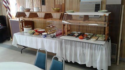 Buffet table with white tablecloths, food displayed. Blue chairs nearby.