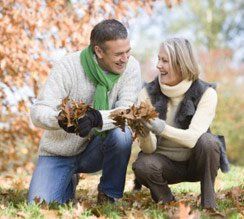 Couple playing with fallen leaves outdoors, smiling.
