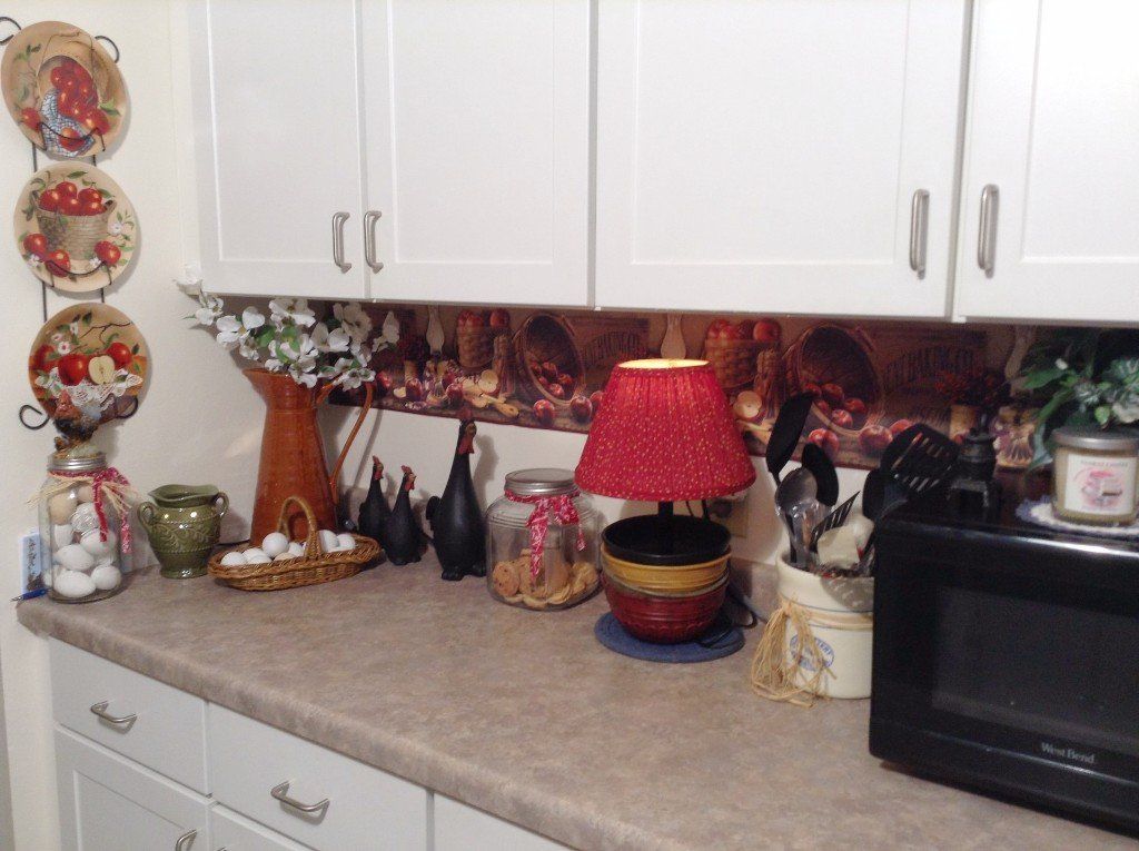 Kitchen countertop with various decorations, including plates, a lamp, and a microwave, set against white cabinets.