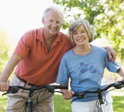 Couple on bikes smiling in a park, man has arm around woman.