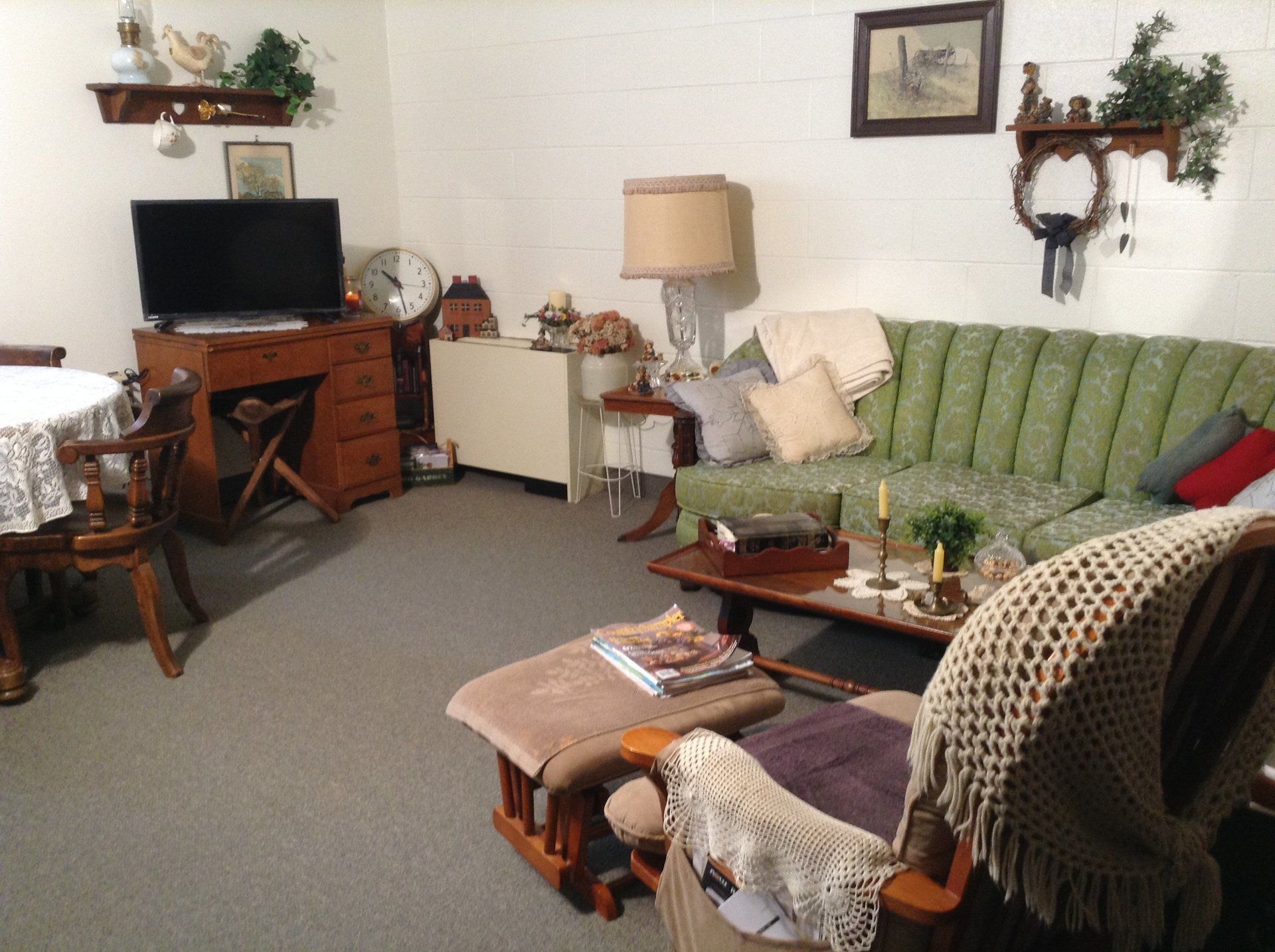 Cozy living room with green sofa, wooden furniture, and vintage decor, featuring a small TV and a rocking chair.