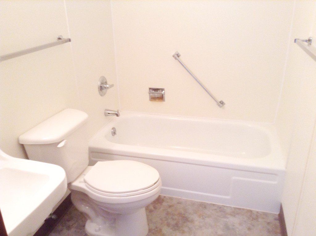 Small bathroom with white toilet, sink, and tub. A silver grab bar is mounted on the wall near the tub.