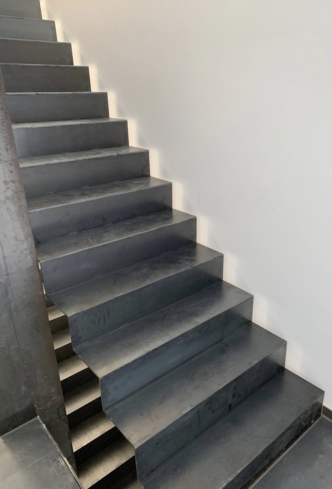 Eine Reihe schwarzer Stufen, die zu einer weißen Wand hinaufführen.