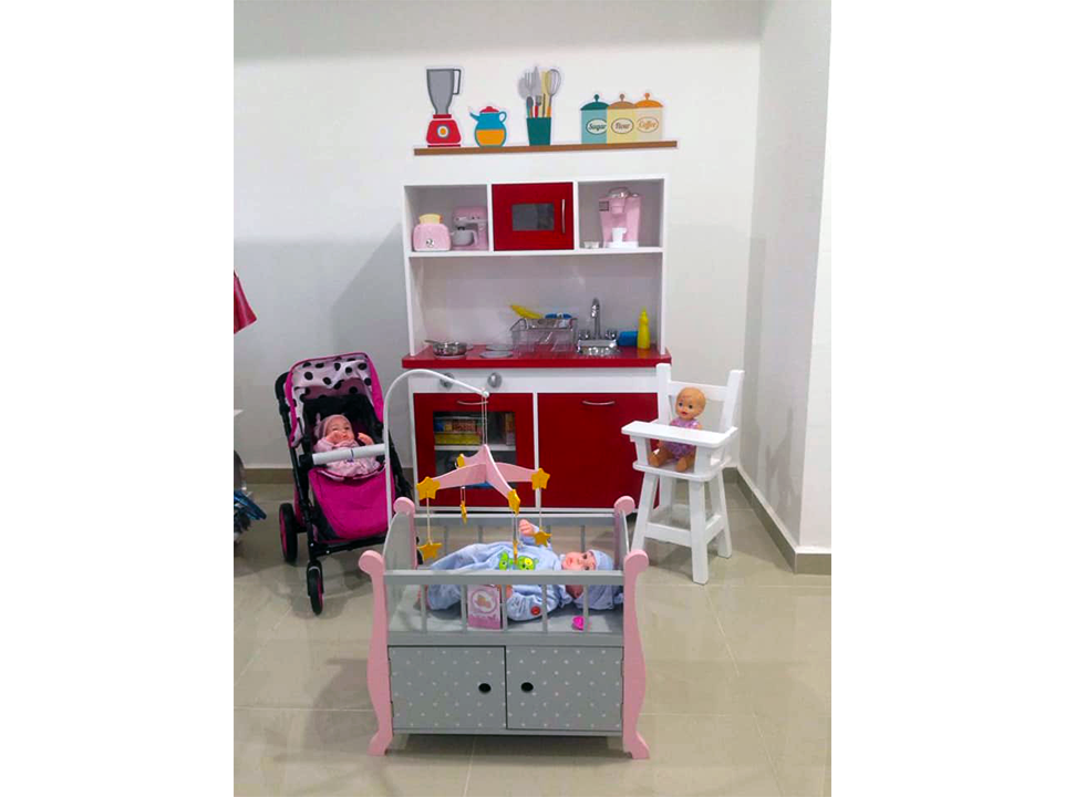 Una habitación con cuna, cochecito, trona y cocina de juguete.