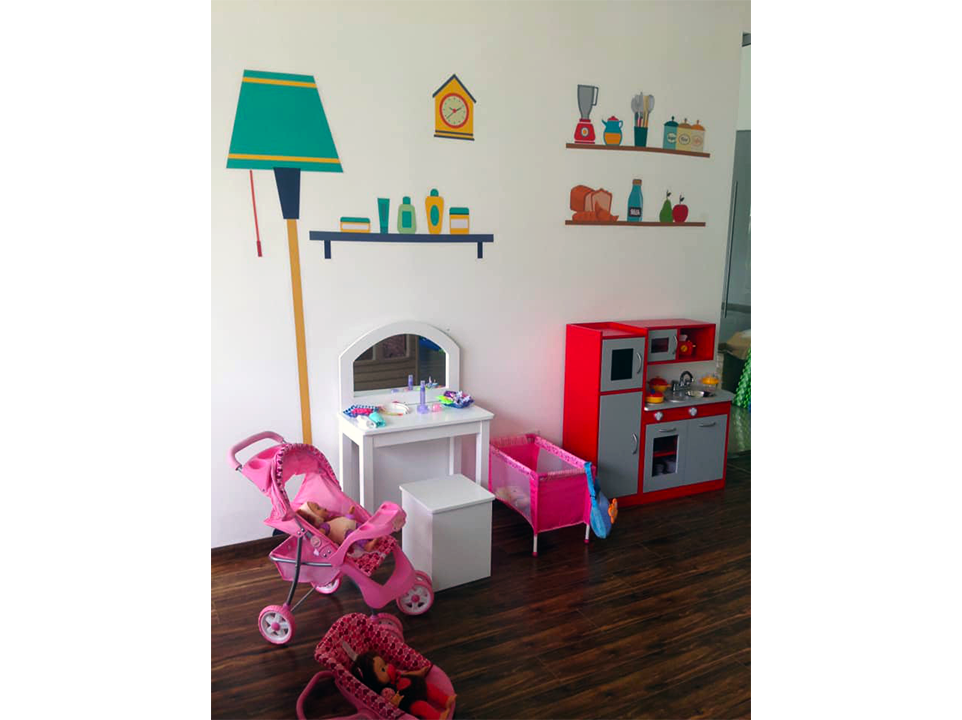 Una habitación con cochecito, cuna, mesa, espejo y lámpara.