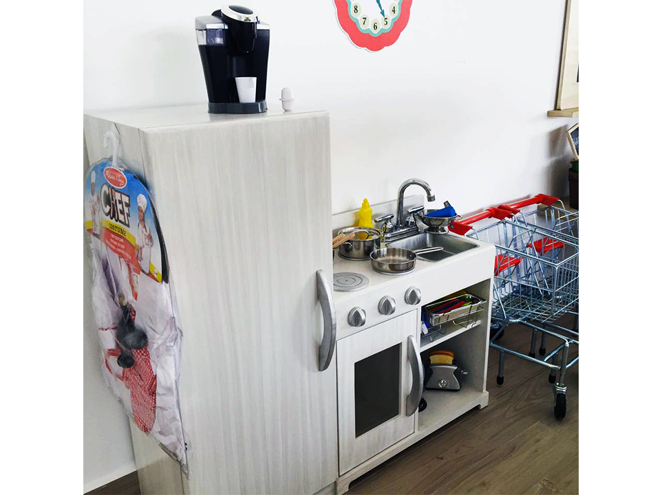 Una cocina de juguete con nevera, fregadero, microondas y carrito de compras.