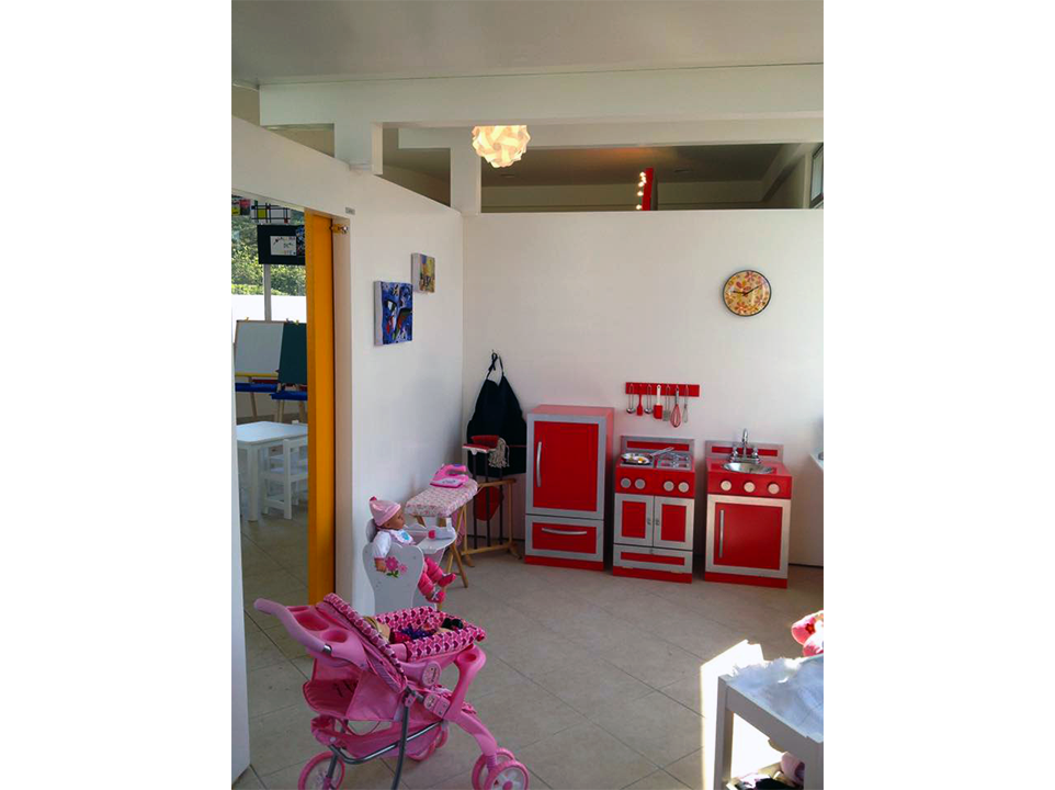 Una habitación con un cochecito rosa y una cocina de juguete roja