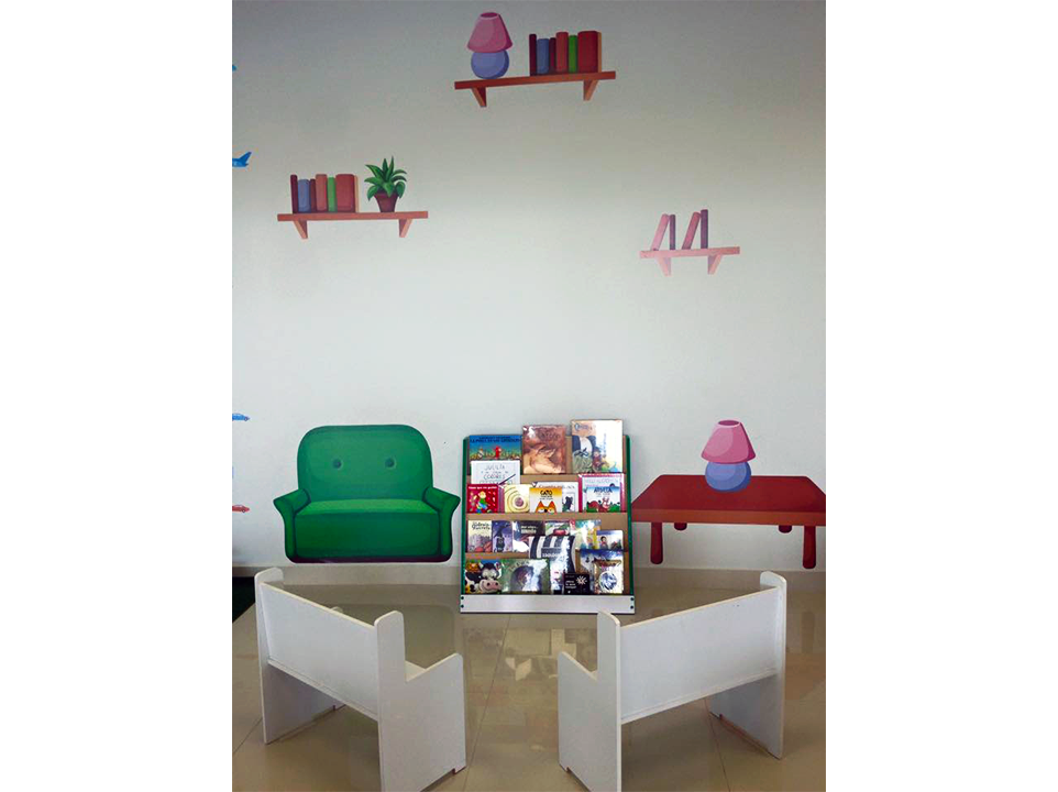 Una habitación infantil con estantería, sillas y mesas.