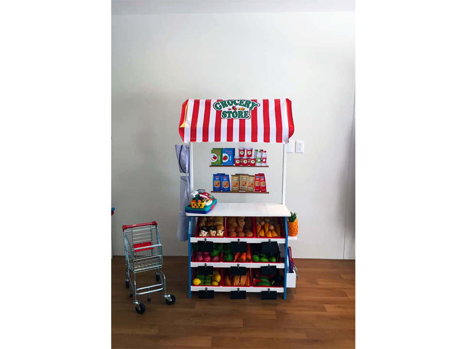 Una tienda de juguetes con un toldo rojo y blanco y un carrito de compras.