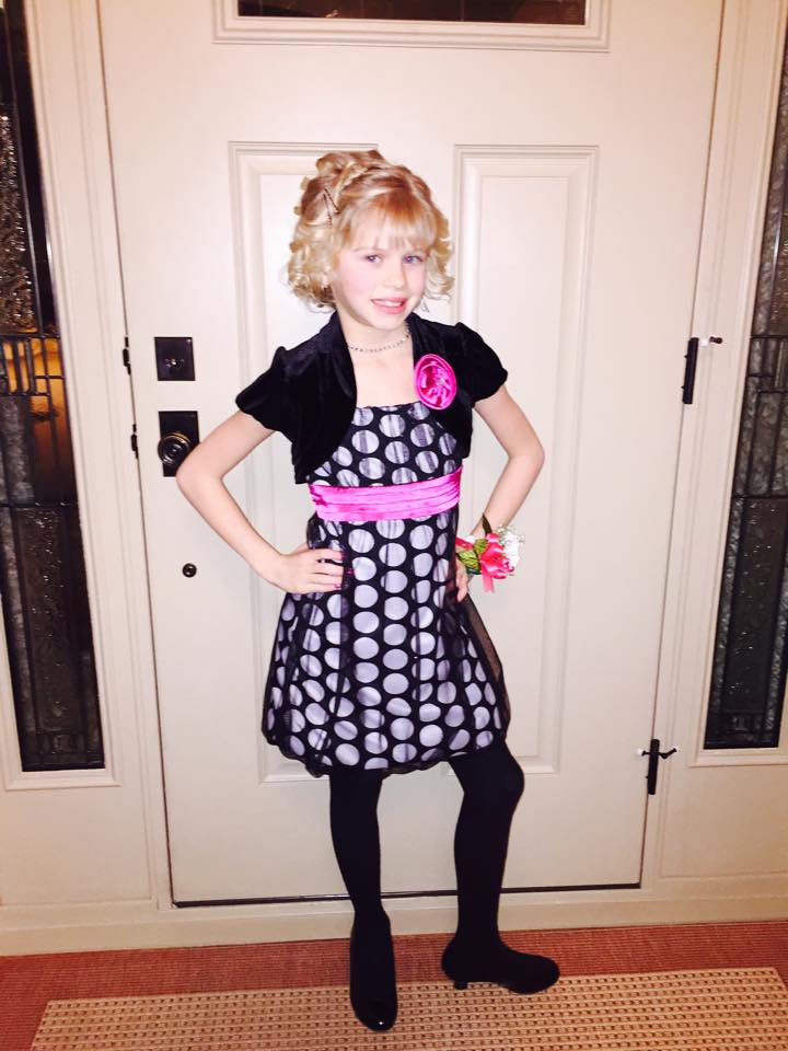 A little girl in a black and white dress is standing in front of a door