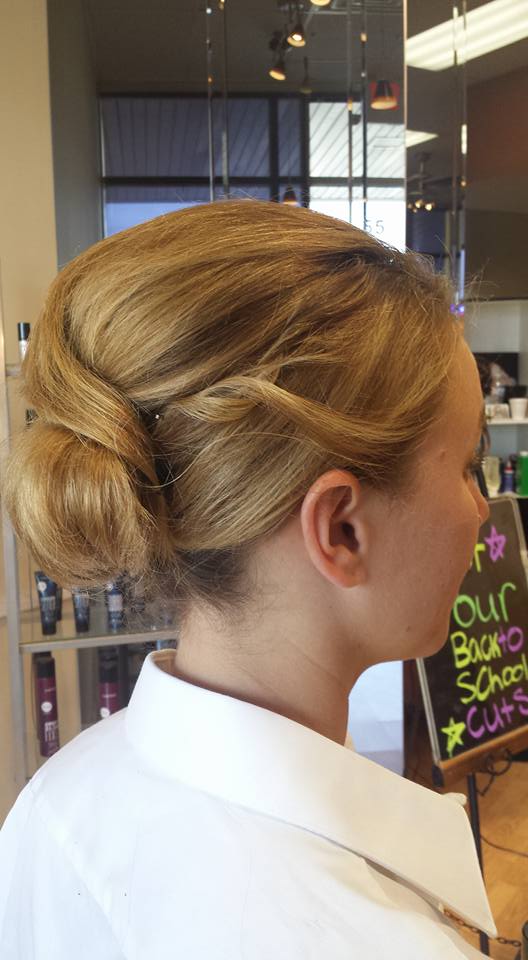 A woman with blonde hair is wearing a white shirt and a bun.
