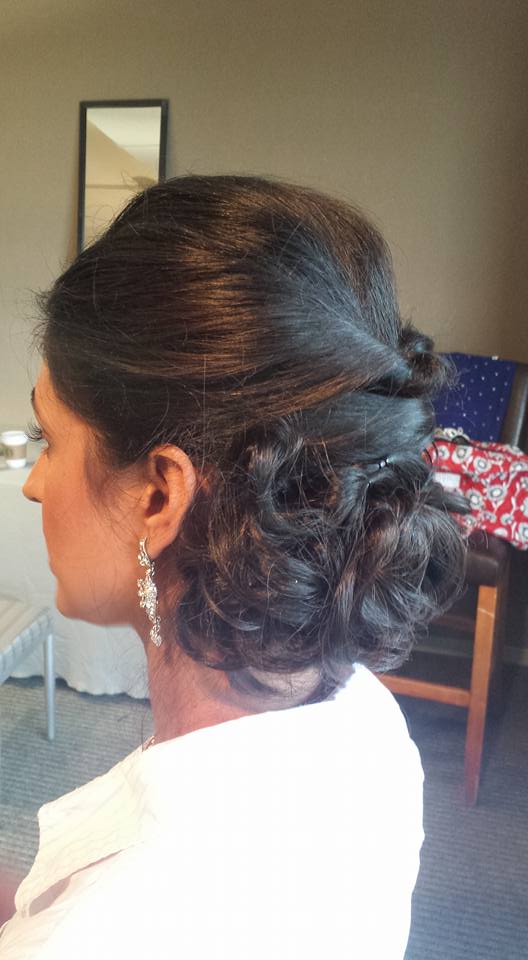 A woman is wearing a white shirt and earrings and has her hair in a bun.