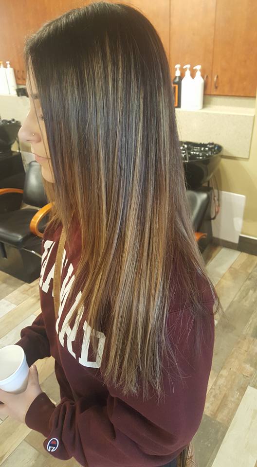 A woman with long hair is standing in a salon holding a cup of coffee.
