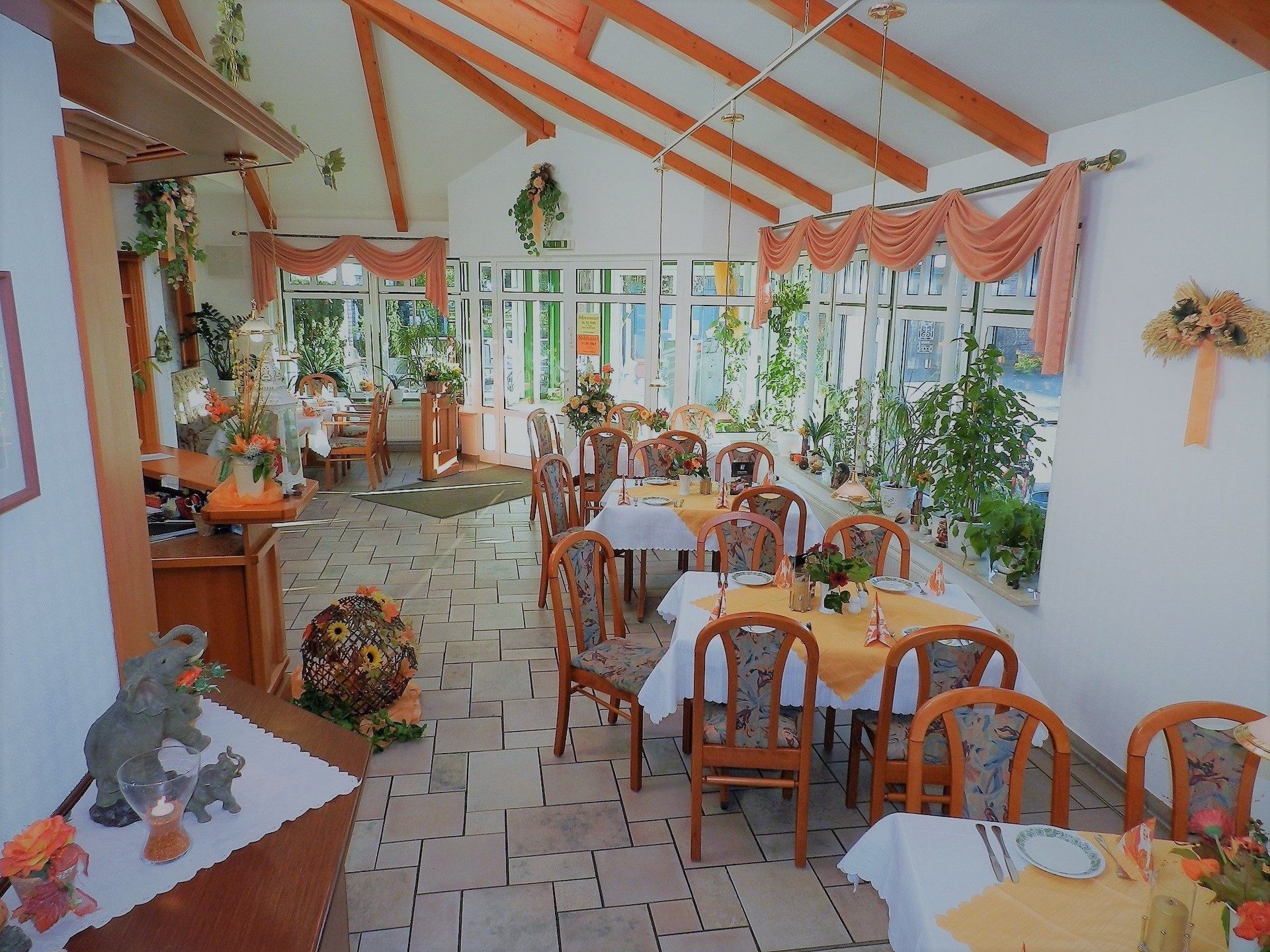 Sonnendurchflutetes Restaurantinnere mit gedeckten Tischen und Blumendekor.