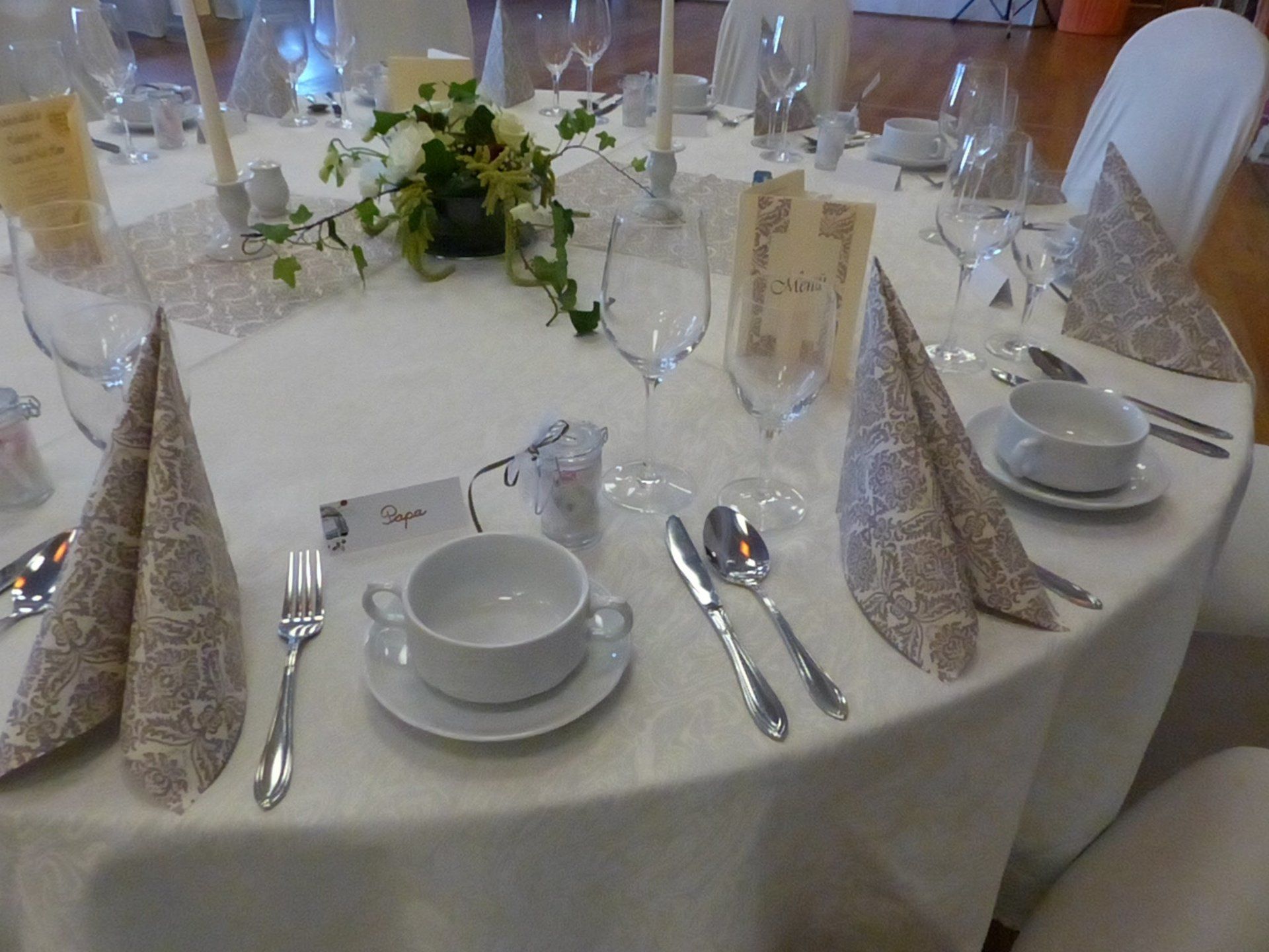 Elegantes rundes Tischset für eine formelle Veranstaltung mit weißer Tischdecke, Besteck, Servietten und Blumendekoration.