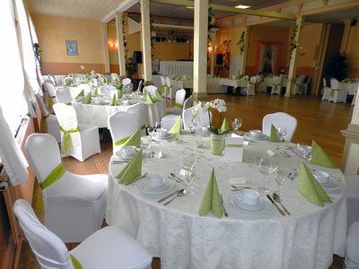 Hochzeitsempfangssaal mit runden Tischen, weißer Tischwäsche, grünen Akzenten und dekorierten Stühlen.