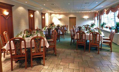 Formeller Speisesaal mit für eine Mahlzeit gedeckten Tischen, braunen Stühlen, weißen Tischdecken und einem Fenster.