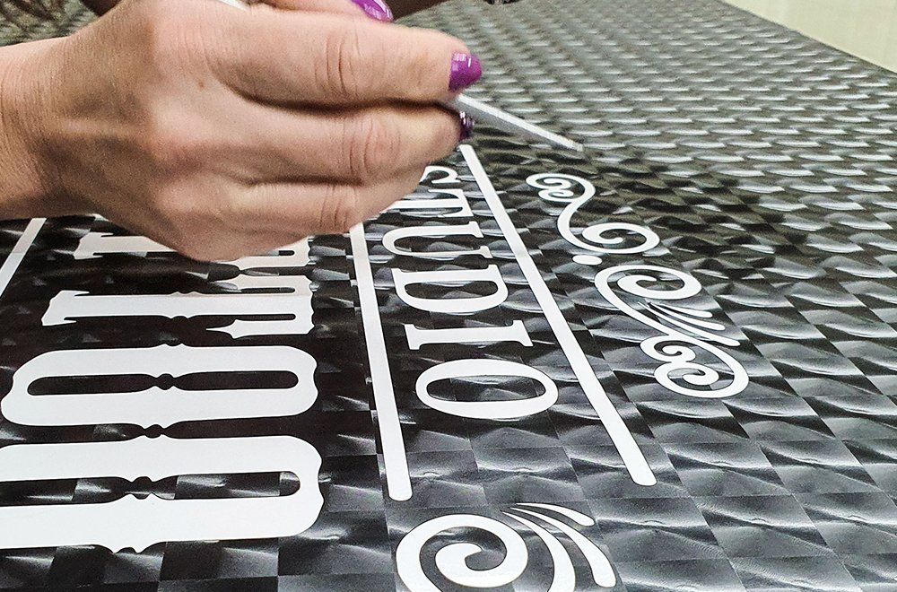 Uma mão com esmalte roxo usa uma ferramenta para aplicar a palavra 